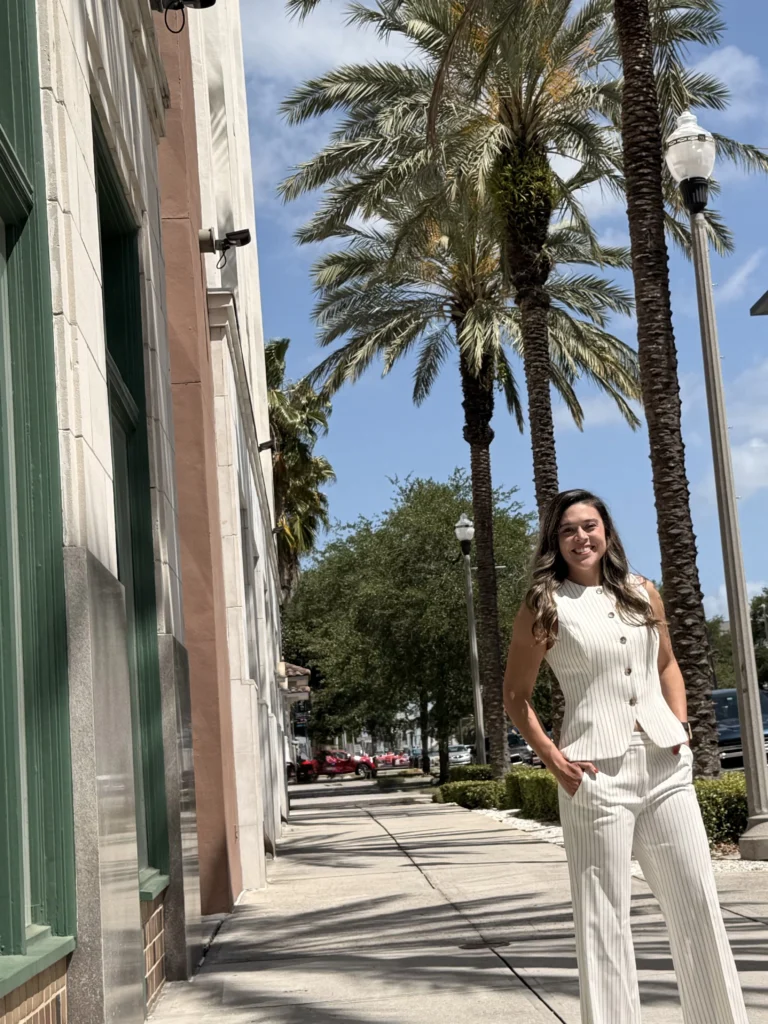 Nikki Savage of Wild Iris Financial standing outdoors on a palm-lined city sidewalk