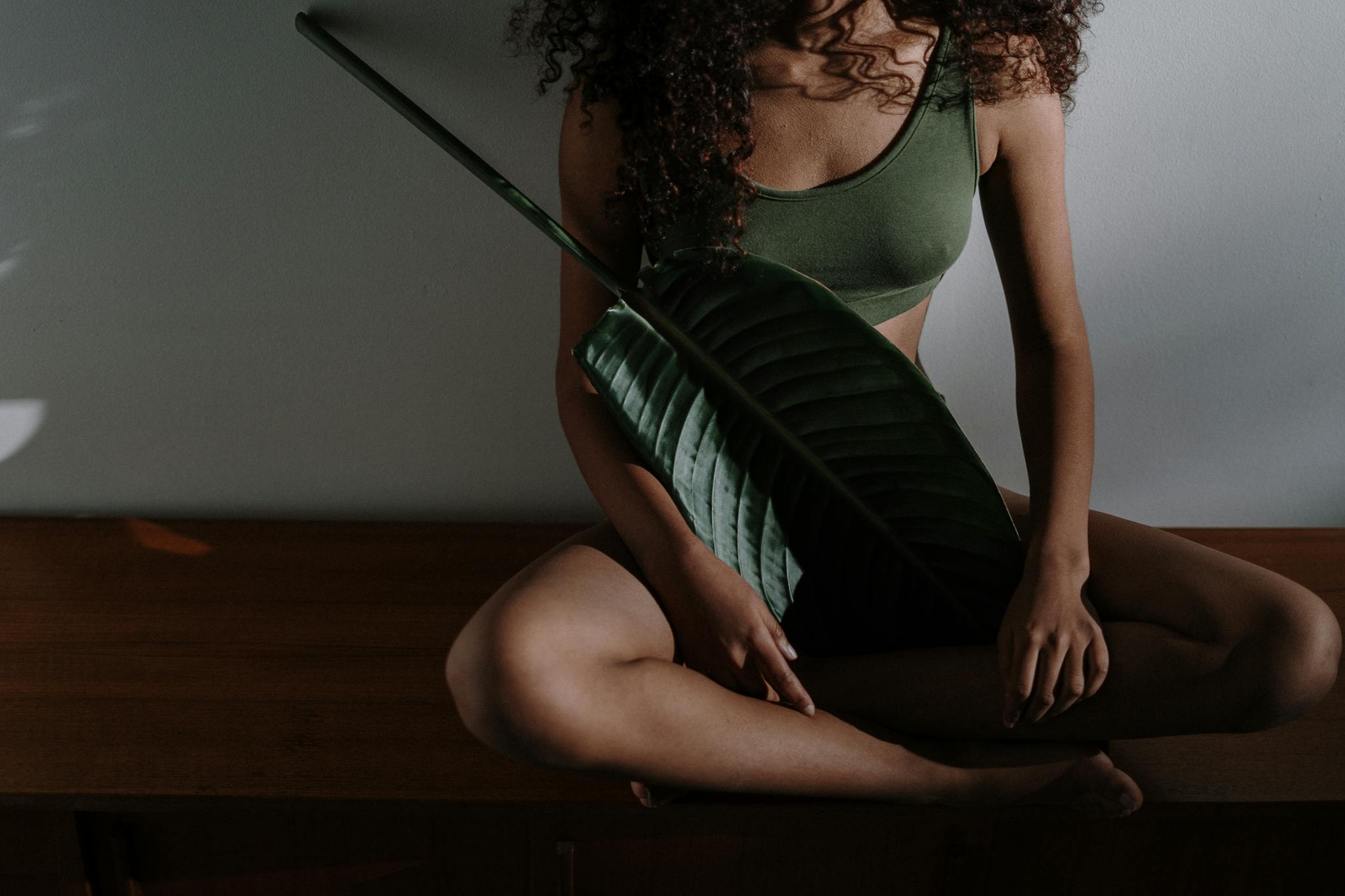 A serene photo of a woman meditating indoors, holding a large tropical leaf.