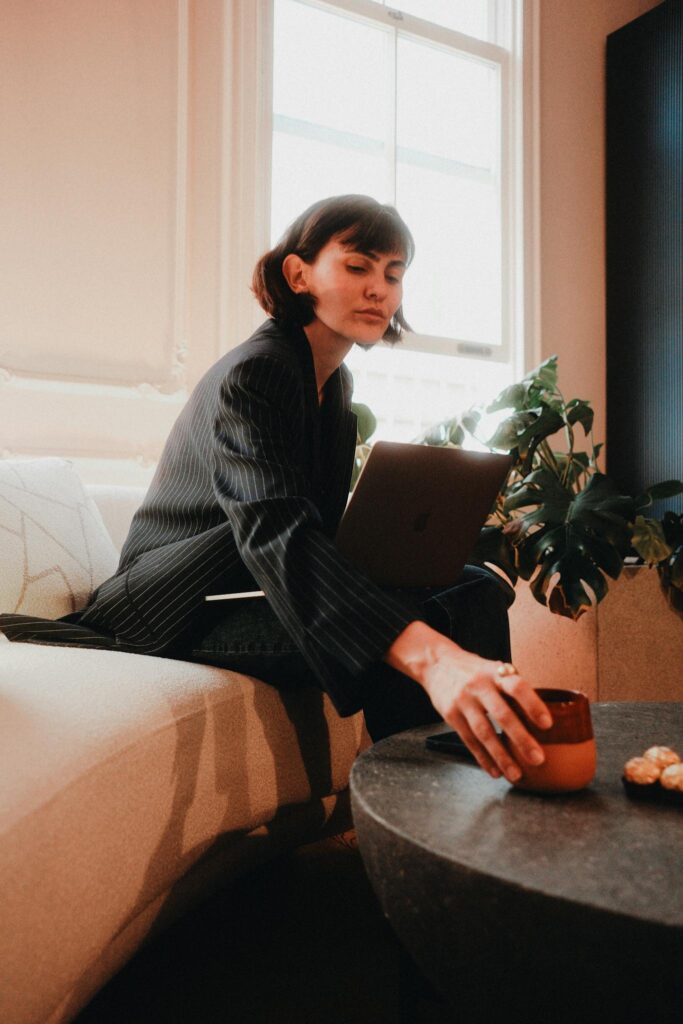 Focused woman in a stylish suit works on a laptop, reaching for coffee.