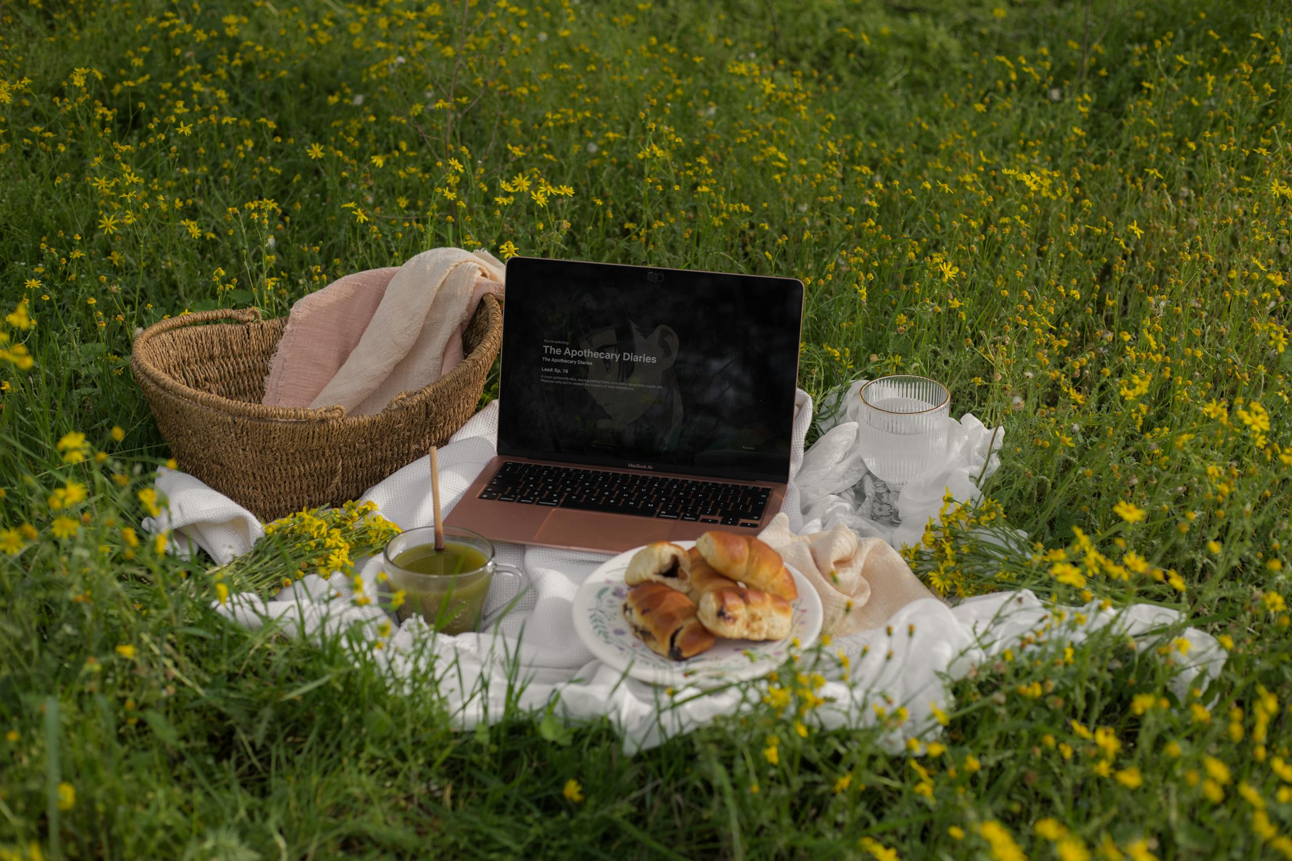 Serene outdoor picnic setup with MacBook Air, pastries, and matcha drink surrounded by blooming spring flowers.