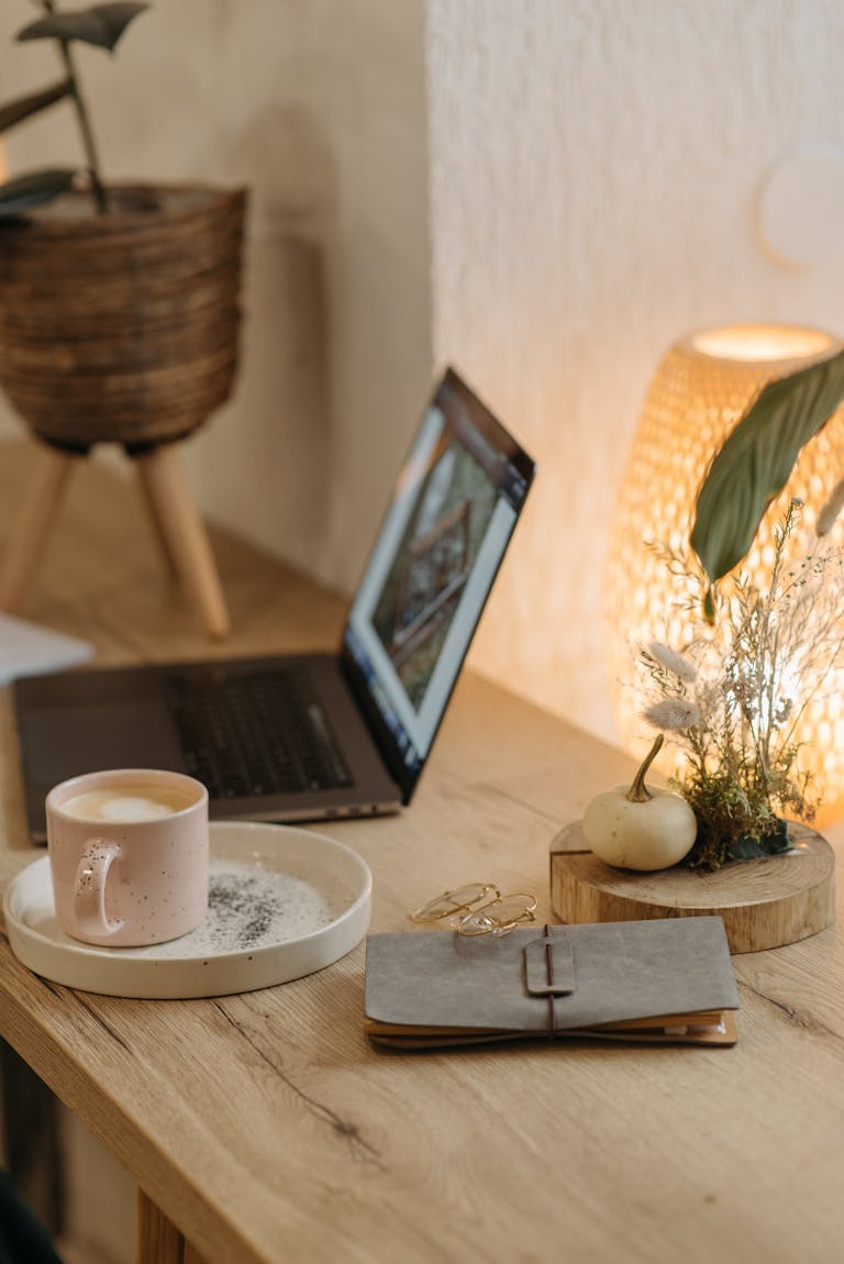 Warm and inviting workspace featuring a coffee cup, laptop, and decor on a wooden table.